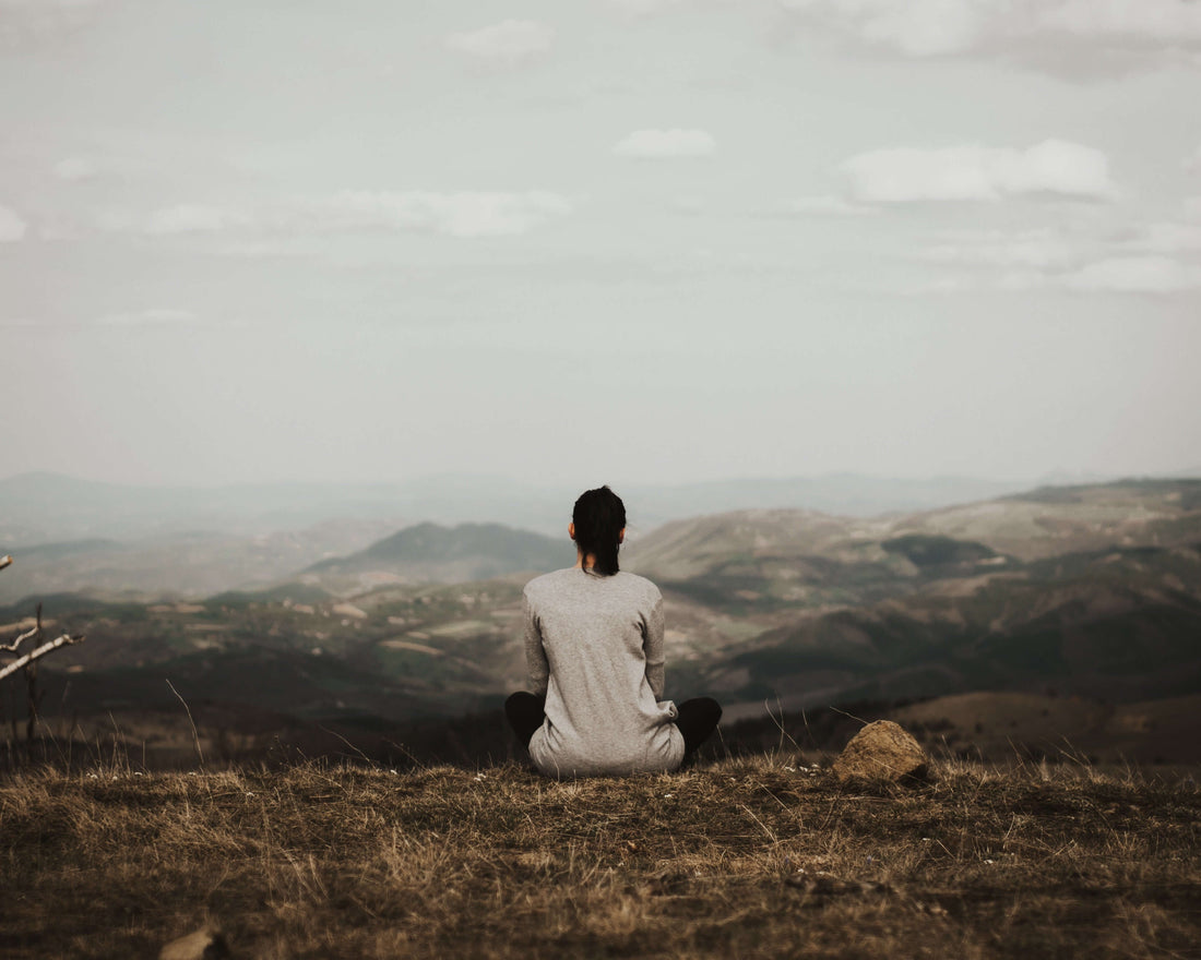 Person practicing mindfulness meditation on a hillside overlooking a vast landscape with mountains and valleys, embodying the calm and focus that mindfulness exercises can bring