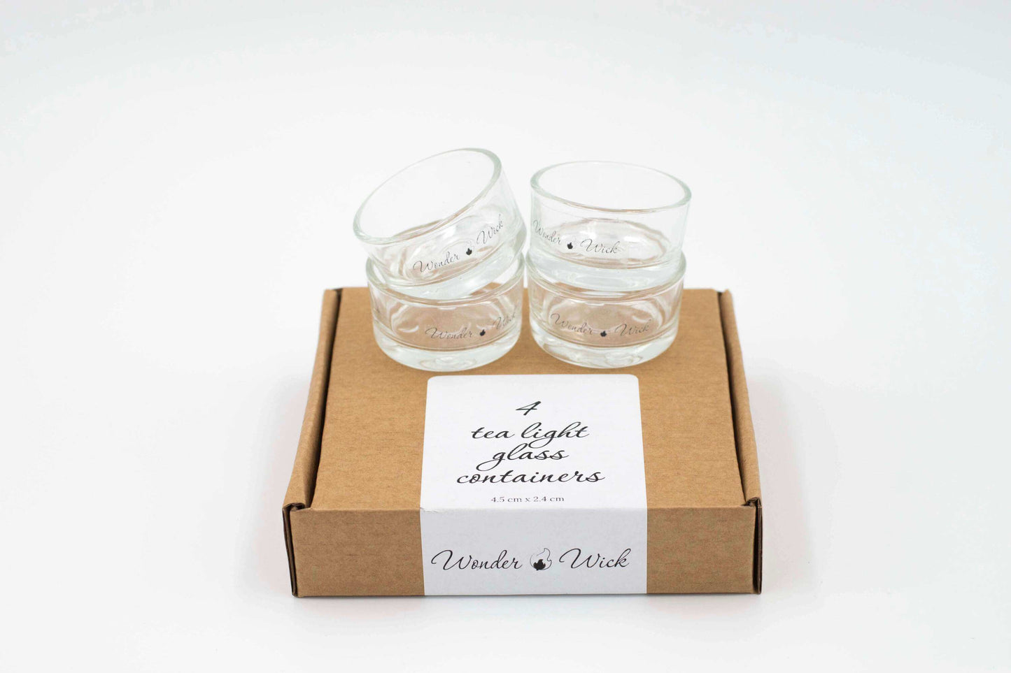 Four glass tea light holders packaged in a cardboard box with shredded paper for protection. The box displays the Wonder Wick logo.