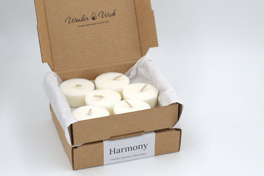 An open box containing 6 Harmony essential oil tealight refills, surrounded by tissue paper. These aromatherapy tealights blend lavender, rosemary, and black pepper to create a soothing, de-stressing ambiance.