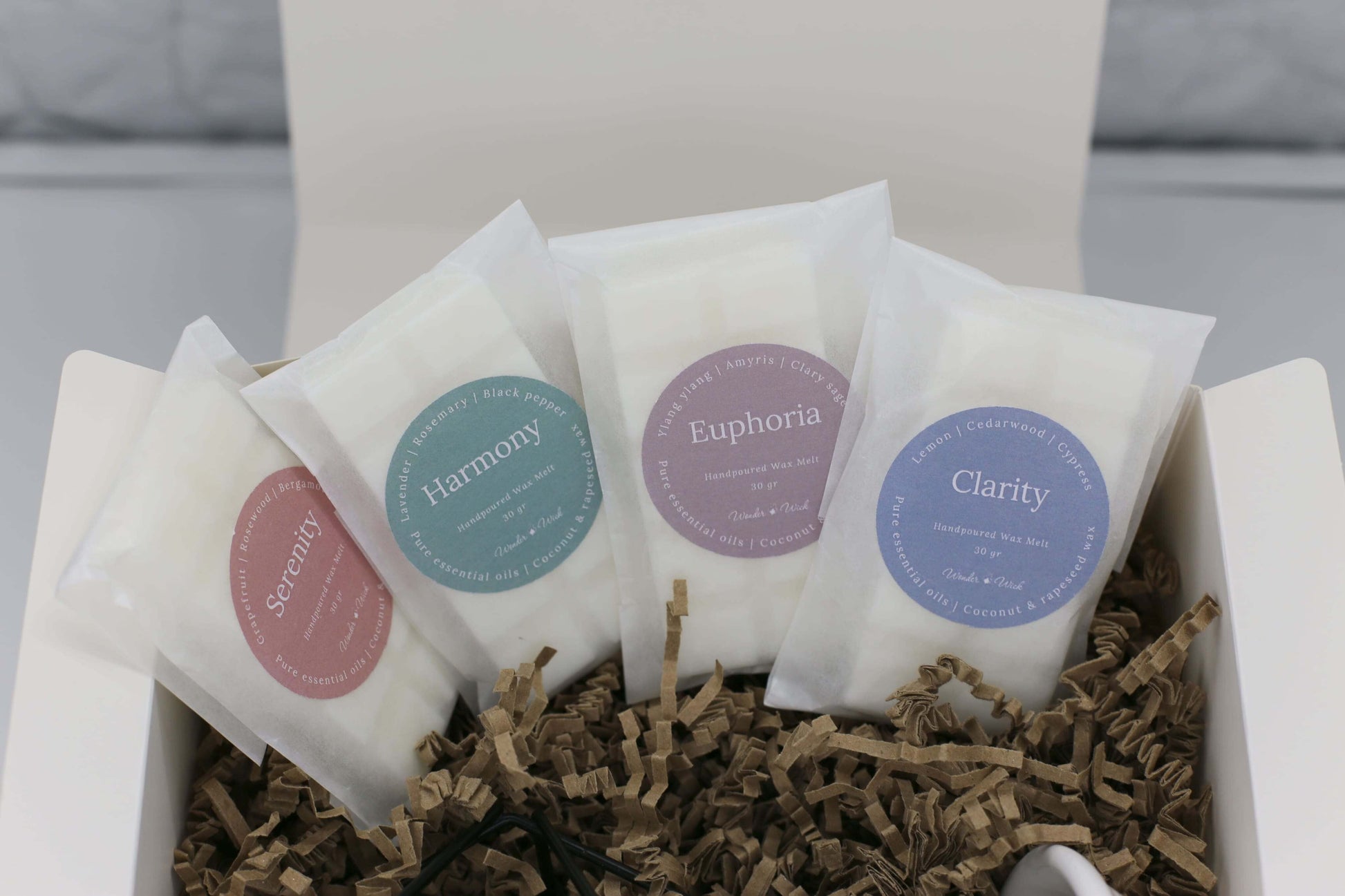 Wonder Wick Wellness Gift Box open with four wax essential oil melts: Serenity, Harmony, Euphoria, and Clarity. Each melt is wrapped in eco-friendly paper, with labels showing scent blends, nestled in crinkle paper.
