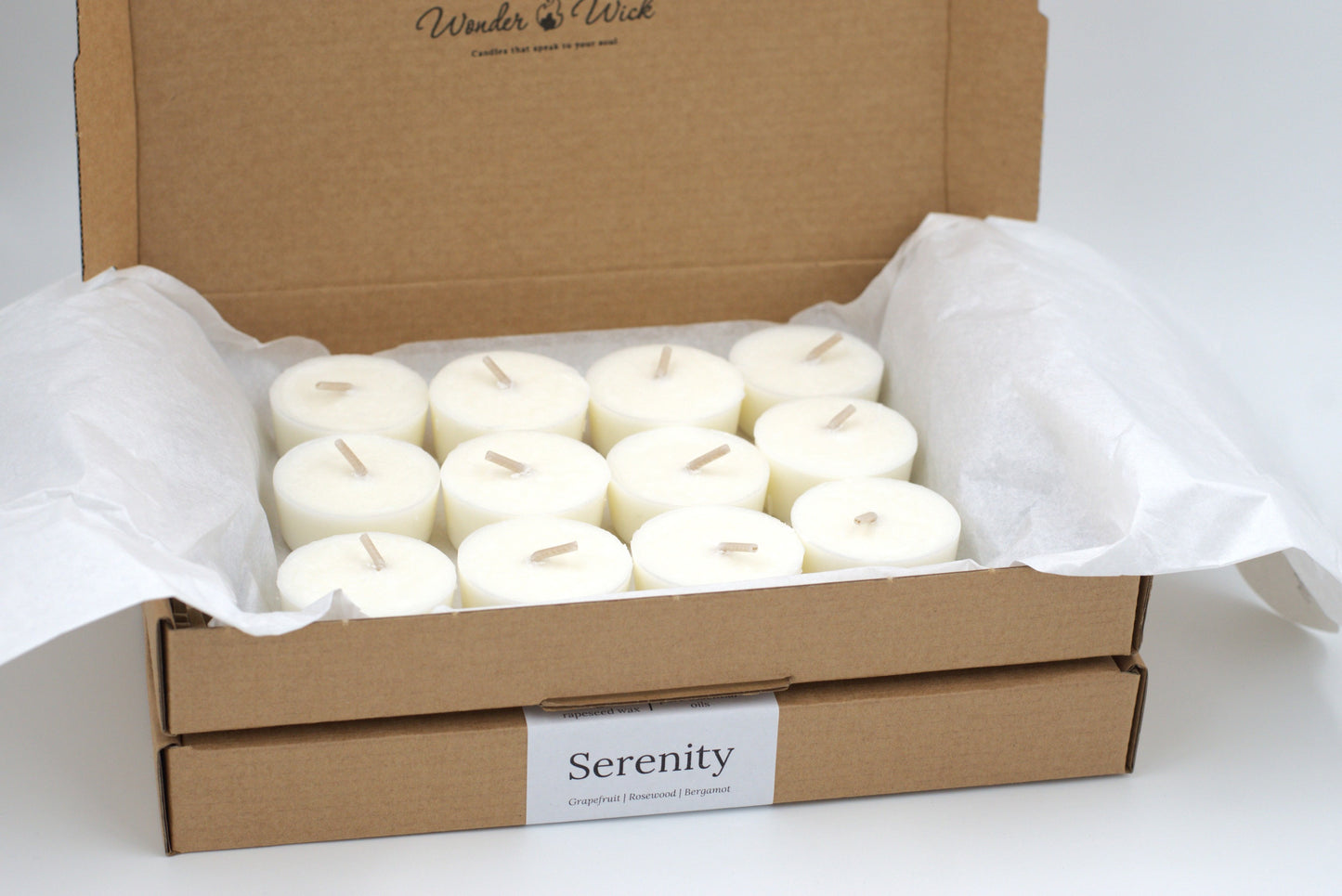 Twelve Serenity tealight refills arranged neatly in an open cardboard box. Made with pure essential oils of grapefruit, rosewood, and bergamot for an uplifting aromatherapy experience.