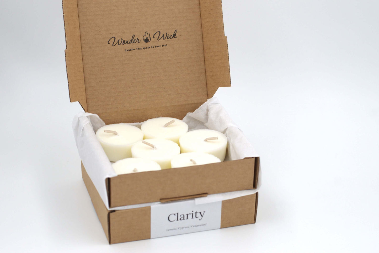 Open cardboard box containing six Clarity essential oil tealight refills by Wonder Wick, made with lemon, cypress and cedarwood and neatly arranged and wrapped in eco-friendly tissue paper. 