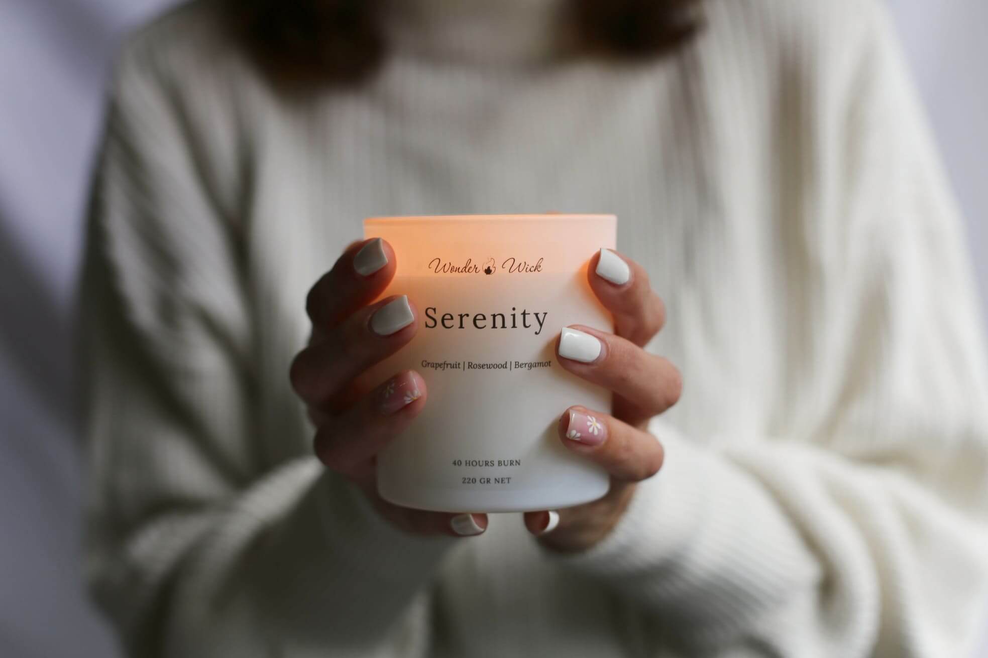 Person holding a lit Wonder Wick Serenity candle with warm, glowing light, showcasing the soothing ambiance of a mindfulness candle made with grapefruit, rosewood, and bergamot essential oils.