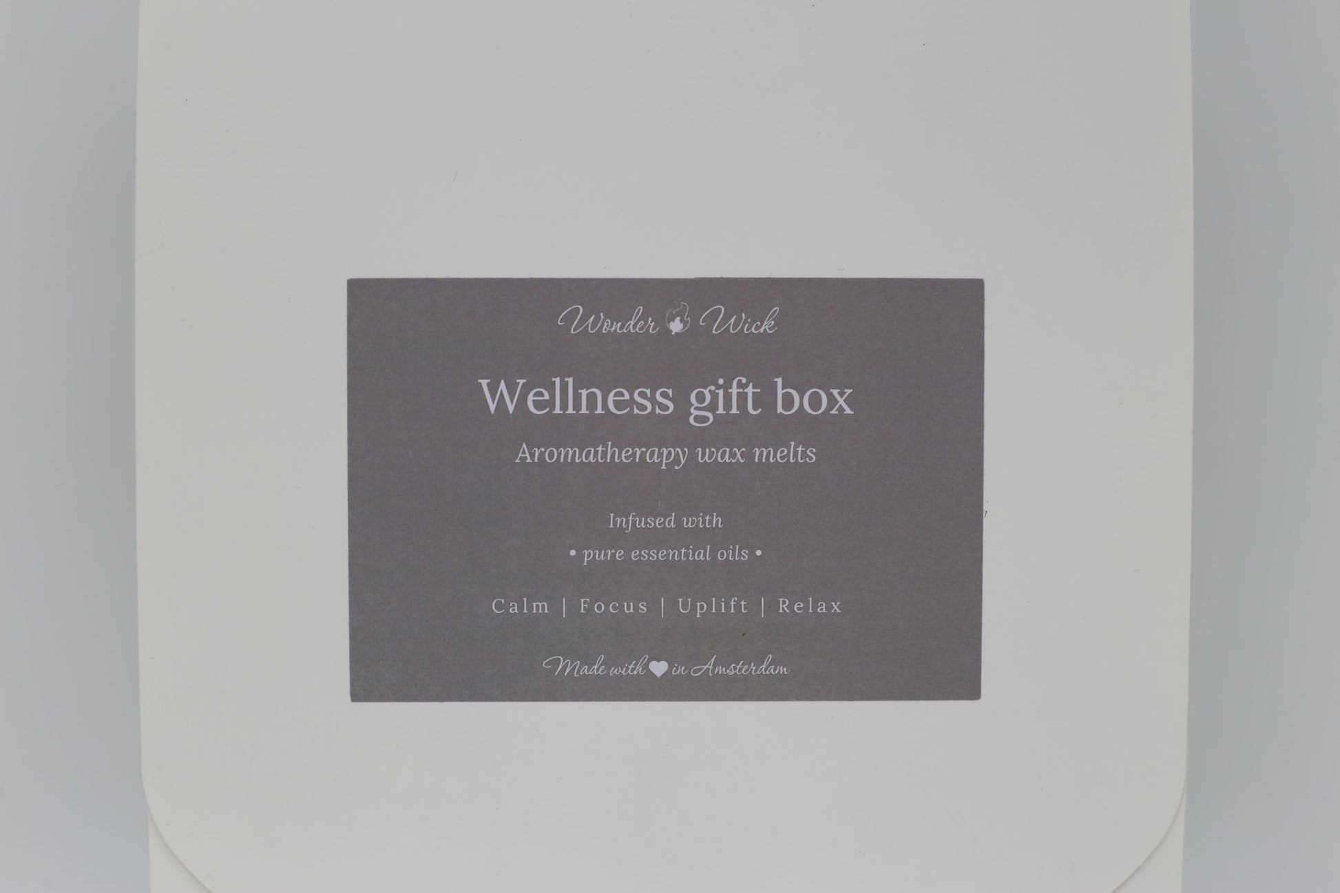 Detailed view of Wonder Wick Wellness Gift Box label for aromatherapy wax melts. Label reads 'Wellness gift box - Aromatherapy wax melts,' with benefits 'Calm, Focus, Uplift, Relax,' and 'Made with love in Amsterdam' in soft gray.