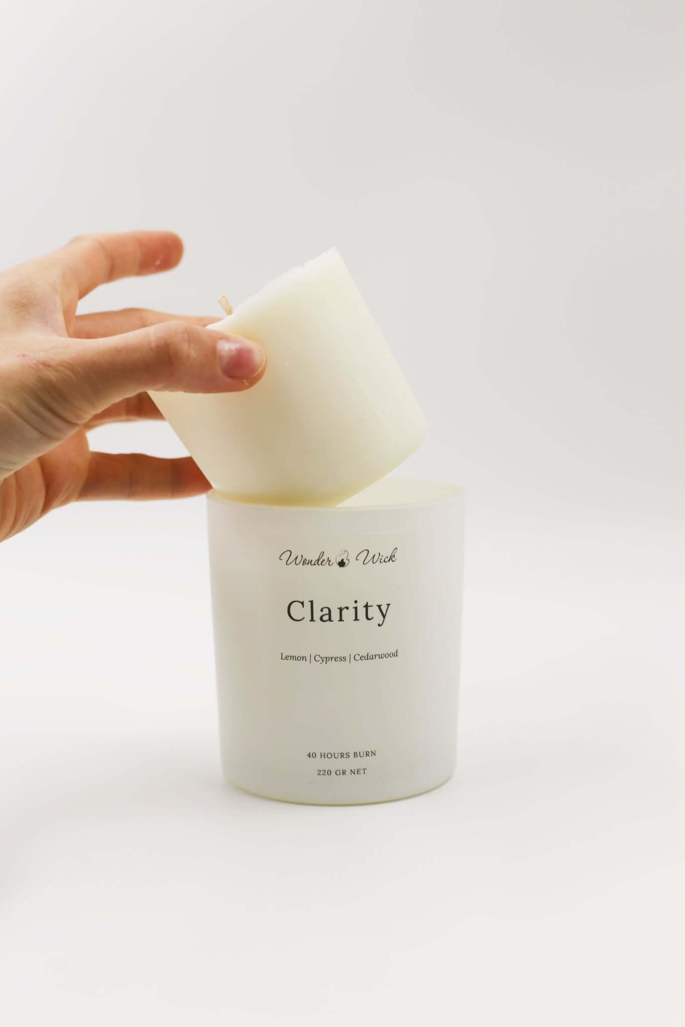 Hand placing a candle refill into Wonder Wick's Clarity jar, illustrating the brand's eco-friendly, refillable design for sustainable candle use.