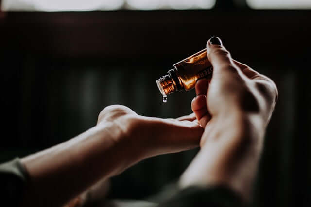 Close-up of hands carefully pouring a drop of essential oil from a brown glass bottle, emphasizing the purity and quality of essential oils used.